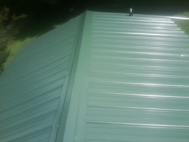 New green metal panels meeting at the ridge of a roof — Flat Roof Repair work by our crew in South Dennis